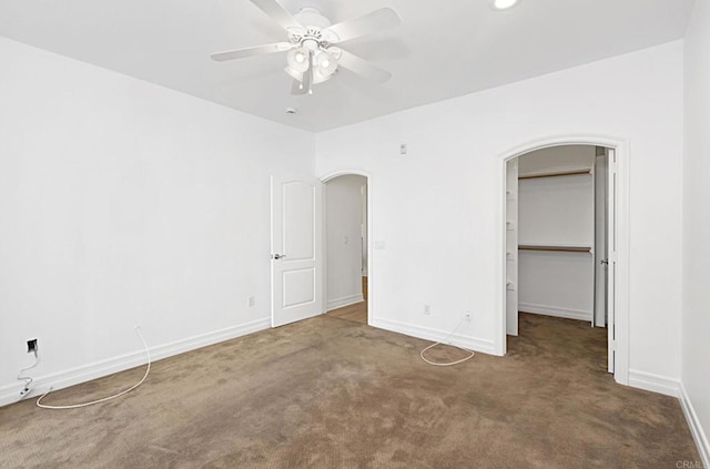 unfurnished bedroom with arched walkways, carpet floors, baseboards, ceiling fan, and a spacious closet