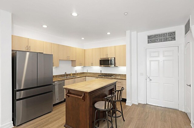 kitchen with light brown cabinetry, stainless steel appliances, light wood-style floors, and a sink