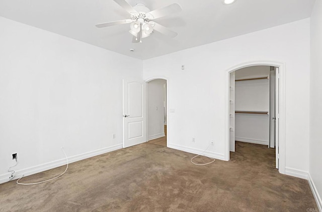 unfurnished bedroom featuring a spacious closet, carpet, arched walkways, and baseboards