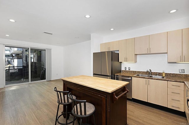 kitchen with a sink, light wood finished floors, light brown cabinetry, and appliances with stainless steel finishes