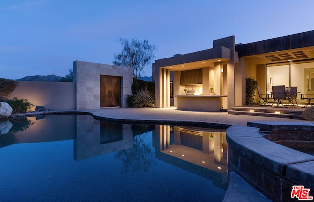 pool at dusk with a mountain view, a patio area, and an in ground hot tub