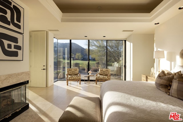 bedroom with floor to ceiling windows, access to outside, a tray ceiling, a mountain view, and a high end fireplace