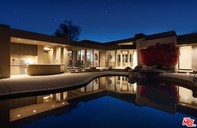 pool at twilight with area for grilling and a patio area