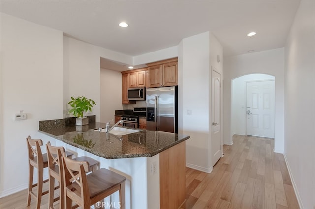 kitchen with sink, light hardwood / wood-style flooring, dark stone counters, kitchen peninsula, and stainless steel appliances