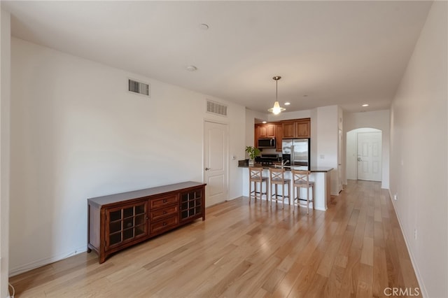 kitchen featuring hanging light fixtures, a kitchen breakfast bar, stainless steel appliances, kitchen peninsula, and light wood-type flooring