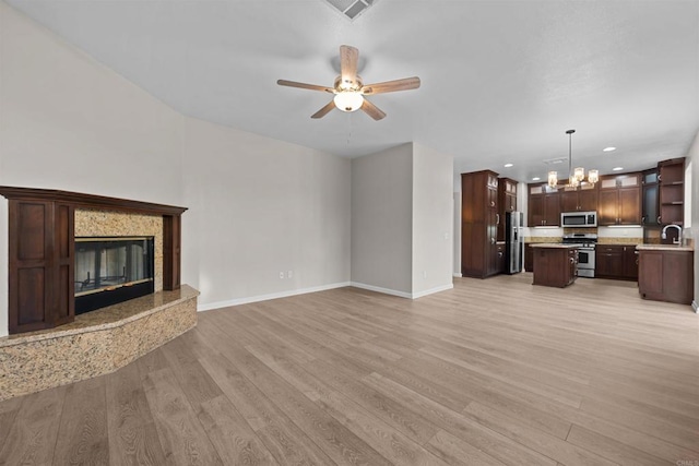 unfurnished living room featuring ceiling fan with notable chandelier, a high end fireplace, sink, and light hardwood / wood-style floors