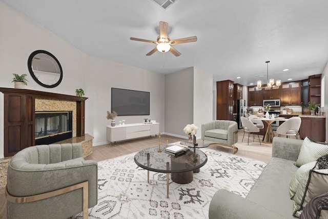 living room featuring ceiling fan with notable chandelier, a tiled fireplace, and light hardwood / wood-style floors