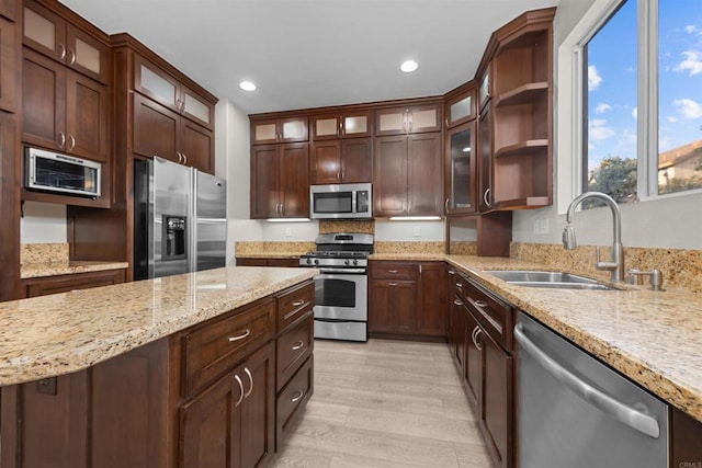 kitchen with sink, dark brown cabinets, appliances with stainless steel finishes, light stone countertops, and light hardwood / wood-style floors