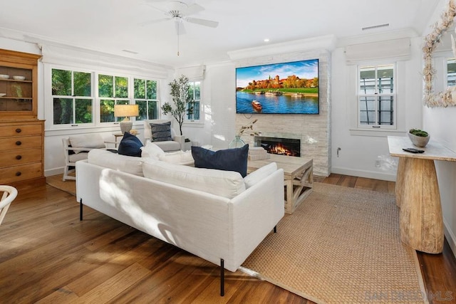 living room featuring hardwood / wood-style flooring, a large fireplace, crown molding, and ceiling fan