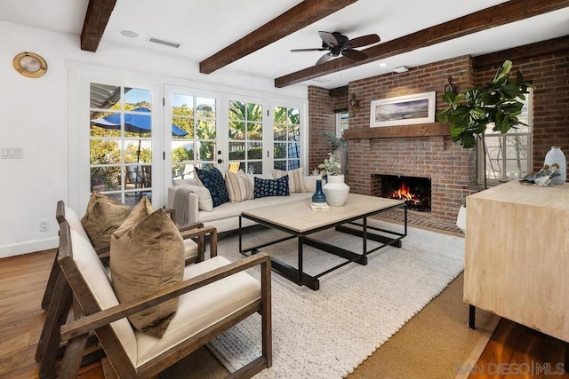 living room with brick wall, beamed ceiling, hardwood / wood-style flooring, ceiling fan, and a brick fireplace