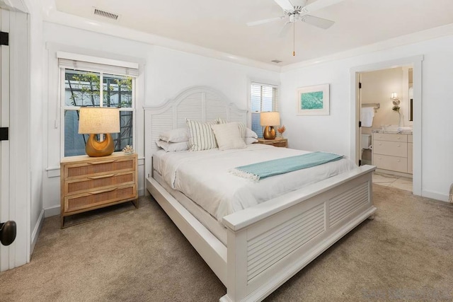 bedroom featuring ceiling fan, light colored carpet, ensuite bath, and multiple windows