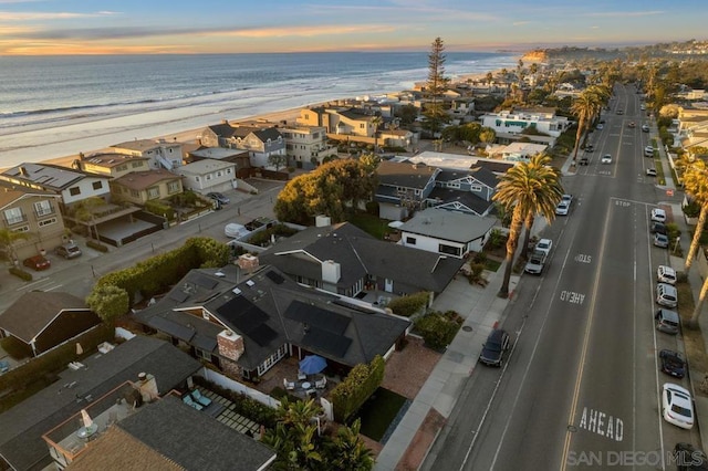 aerial view at dusk featuring a water view and a beach view