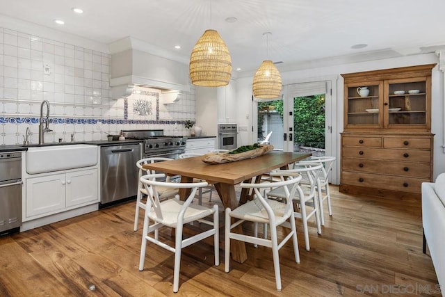 kitchen with pendant lighting, white cabinetry, sink, stainless steel appliances, and light hardwood / wood-style flooring