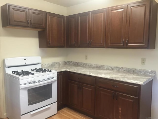 kitchen with light wood-type flooring, white range with gas stovetop, and dark brown cabinetry