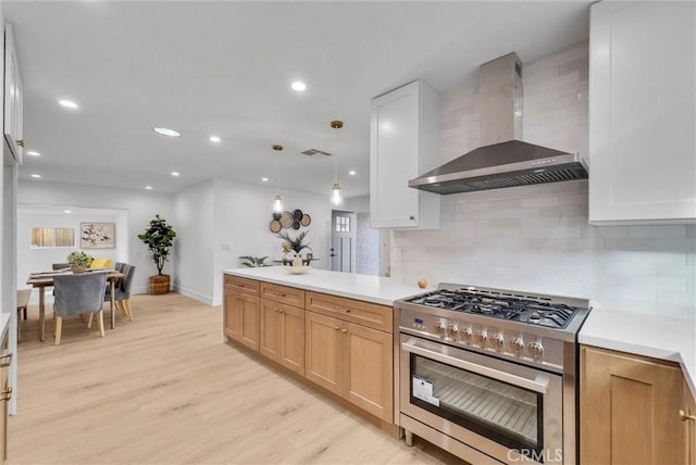 kitchen with pendant lighting, light brown cabinetry, wall chimney exhaust hood, stainless steel gas range, and light hardwood / wood-style flooring