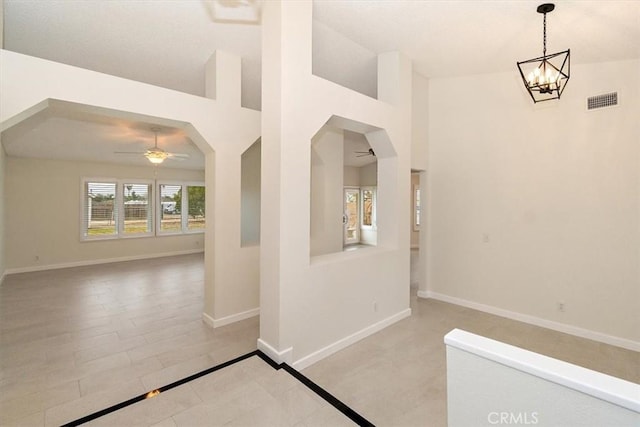 empty room with ceiling fan with notable chandelier and a high ceiling