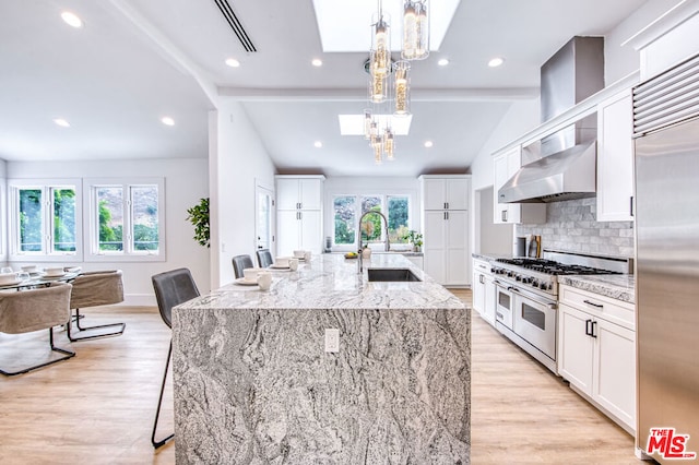 kitchen with sink, hanging light fixtures, premium appliances, light stone countertops, and a center island with sink