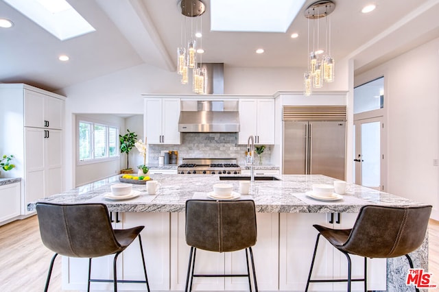 kitchen featuring white cabinets, decorative light fixtures, stainless steel built in fridge, and a large island with sink