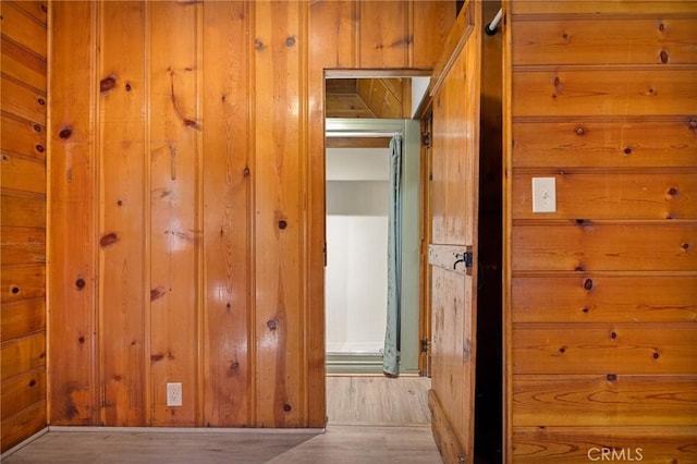 hallway with light hardwood / wood-style flooring and wood walls