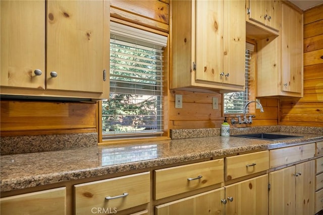 kitchen featuring a healthy amount of sunlight, wooden walls, light brown cabinetry, and sink