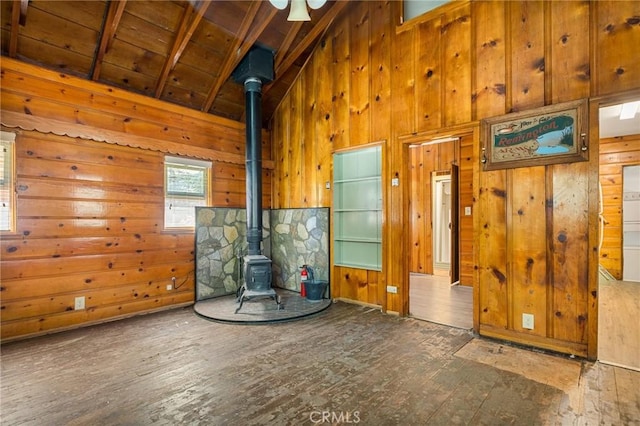 unfurnished living room with a wood stove, beam ceiling, dark hardwood / wood-style floors, wooden ceiling, and wood walls