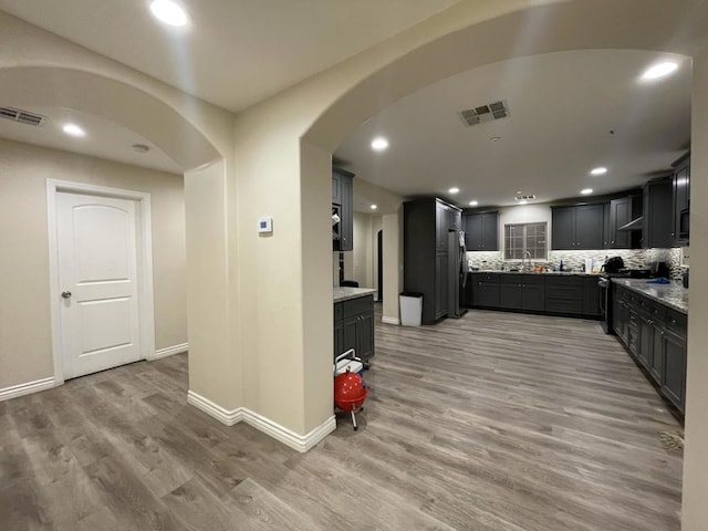 kitchen with tasteful backsplash, light stone countertops, stainless steel appliances, and hardwood / wood-style floors