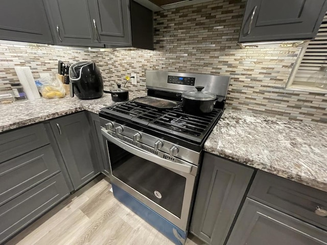 kitchen with gray cabinets, tasteful backsplash, gas stove, light stone countertops, and light hardwood / wood-style flooring