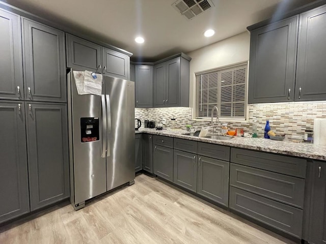 kitchen with light stone countertops, sink, light hardwood / wood-style flooring, and stainless steel fridge with ice dispenser