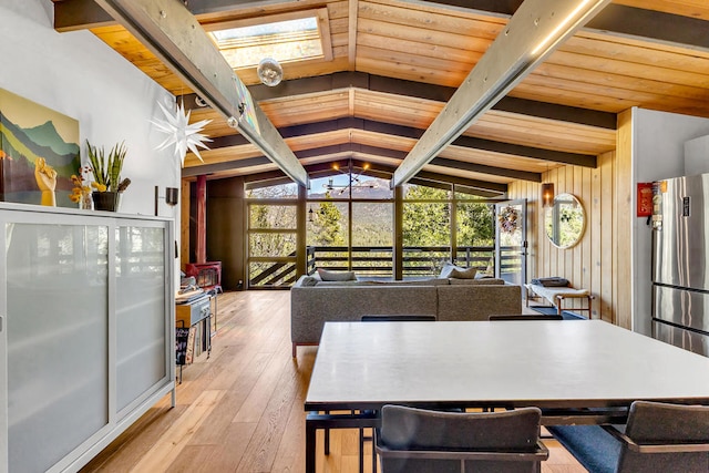 dining space with wooden walls, vaulted ceiling with beams, a wealth of natural light, and light hardwood / wood-style floors