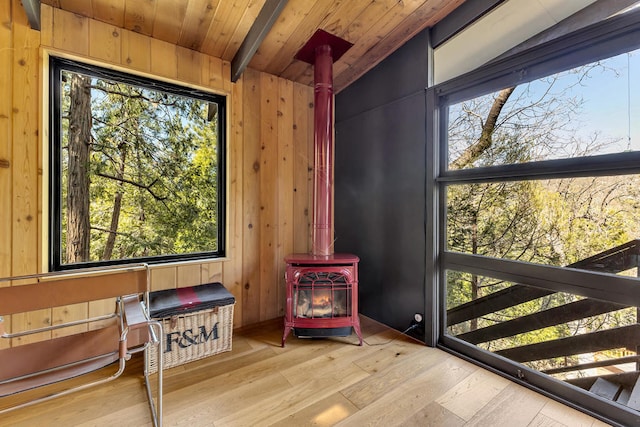 sunroom / solarium featuring a healthy amount of sunlight, lofted ceiling, a wood stove, and wooden ceiling