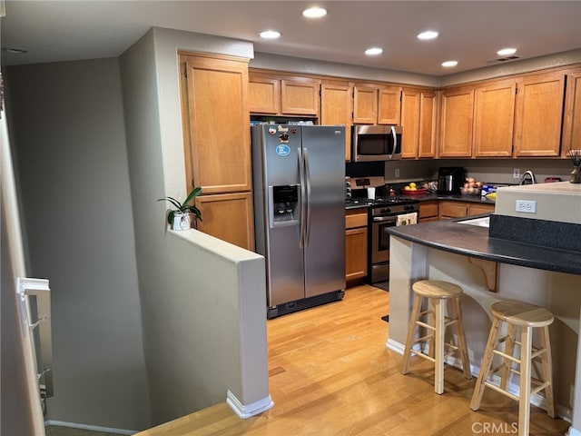 kitchen featuring a breakfast bar area, stainless steel appliances, light wood-style floors, brown cabinets, and dark countertops