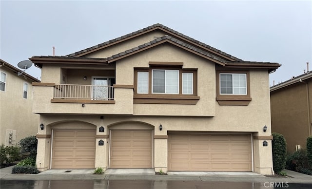 townhome / multi-family property featuring a garage, a tile roof, a balcony, and stucco siding