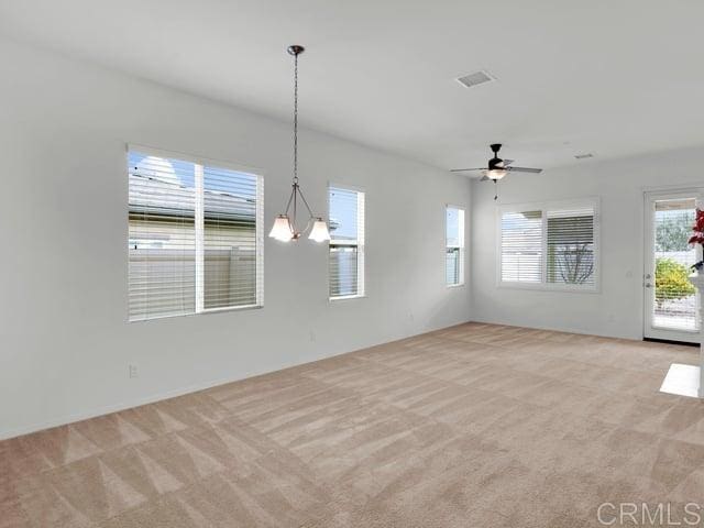 empty room with ceiling fan with notable chandelier and light carpet