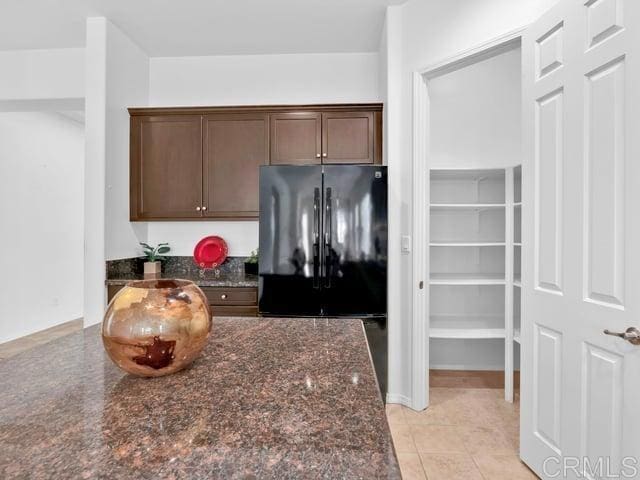 kitchen with light tile patterned flooring, black refrigerator, dark stone countertops, and dark brown cabinetry