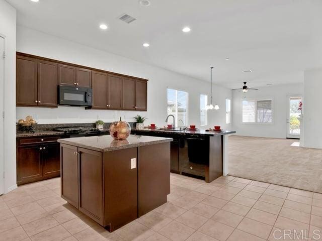 kitchen with a kitchen island, dark stone countertops, hanging light fixtures, black appliances, and light carpet