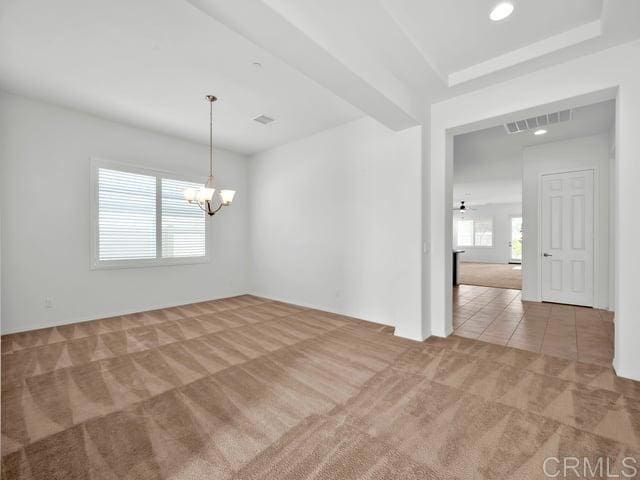 carpeted spare room with an inviting chandelier