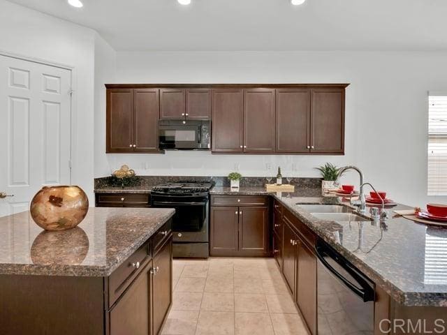 kitchen with dark brown cabinetry, sink, light tile patterned floors, dark stone counters, and stainless steel appliances