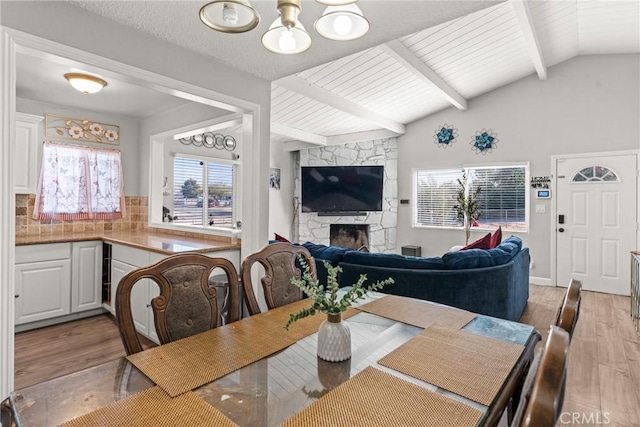 dining room with vaulted ceiling with beams, a fireplace, light hardwood / wood-style floors, and a chandelier