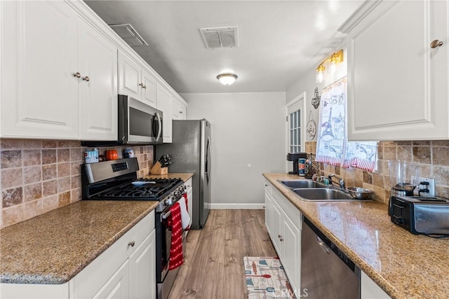 kitchen with appliances with stainless steel finishes, white cabinetry, sink, decorative backsplash, and light stone counters