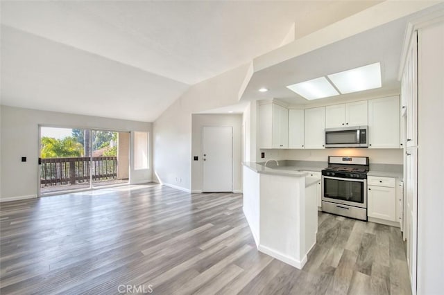 kitchen with vaulted ceiling, white cabinetry, appliances with stainless steel finishes, and light hardwood / wood-style flooring