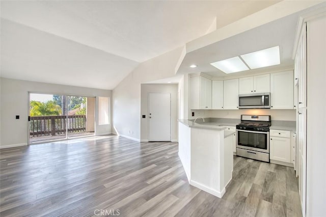 kitchen with stainless steel appliances, vaulted ceiling, white cabinets, and light hardwood / wood-style flooring