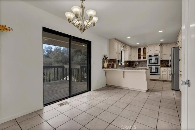 kitchen featuring light tile patterned floors, appliances with stainless steel finishes, backsplash, decorative light fixtures, and kitchen peninsula