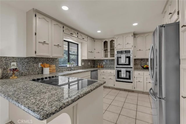 kitchen featuring sink, stone countertops, light tile patterned floors, kitchen peninsula, and stainless steel appliances