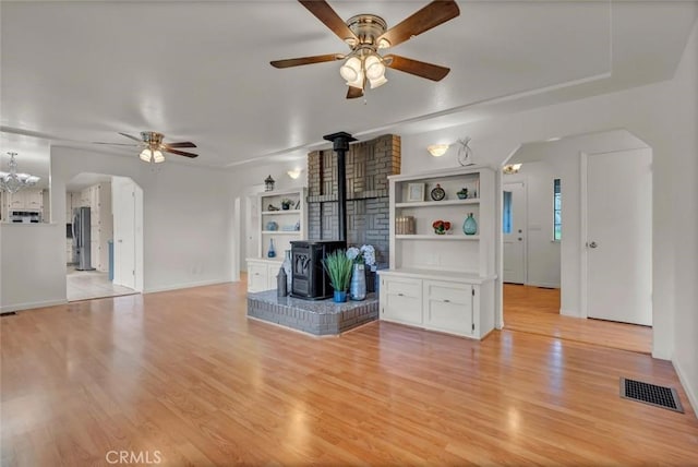 unfurnished living room with a wood stove, ceiling fan, and light hardwood / wood-style flooring