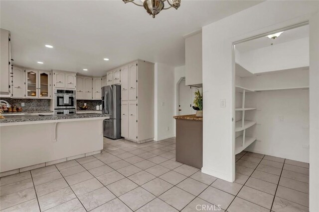 kitchen with light tile patterned flooring, tasteful backsplash, sink, kitchen peninsula, and stainless steel appliances