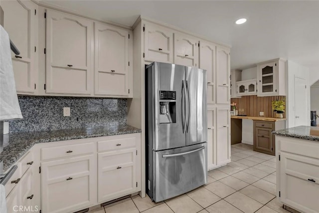 kitchen with tasteful backsplash, dark stone countertops, white cabinets, light tile patterned floors, and stainless steel refrigerator with ice dispenser