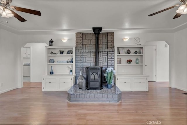 unfurnished living room featuring ceiling fan, light hardwood / wood-style flooring, and a wood stove