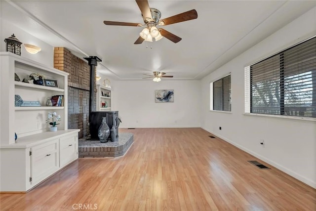 unfurnished living room featuring ceiling fan, light wood-type flooring, built in features, and a wood stove