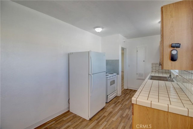 kitchen with sink, tile counters, white appliances, and light hardwood / wood-style floors