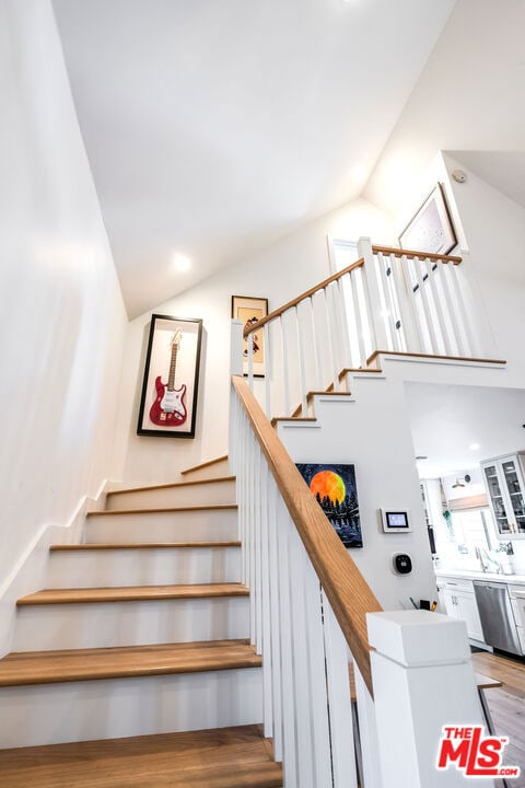 stairway with hardwood / wood-style flooring and high vaulted ceiling